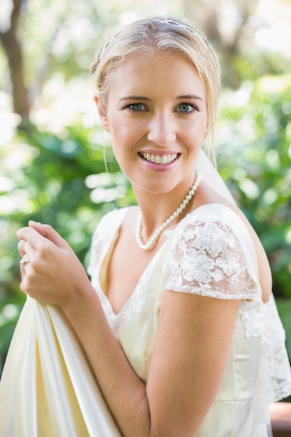 Sorrindo noiva loira segurando seu vestido olhando a câmera