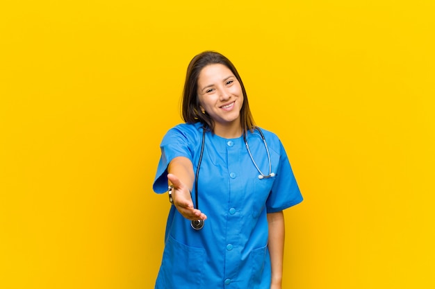 Sorrindo, olhando feliz, confiante e amigável, oferecendo um aperto de mão para fechar um acordo de cooperação isolado contra a parede amarela