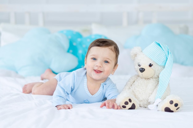 Sorrindo ou rindo bebê na cama para dormir com ursinho de pelúcia, interior do quarto do bebê, bebê feliz e saudável