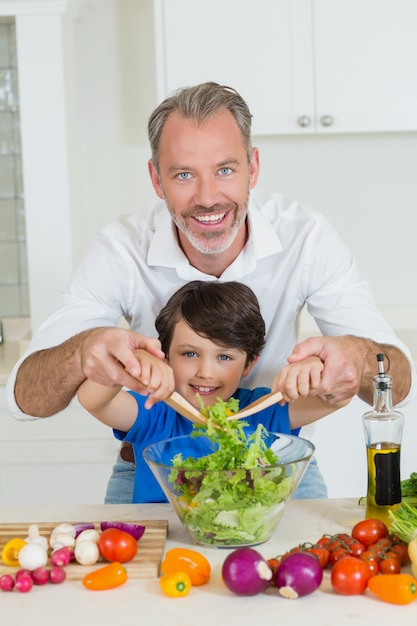 Sorrindo pai e filho preparando salada na cozinha em casa