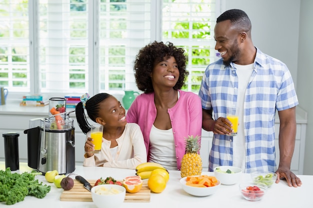 Sorrindo, pais e filha tomando um copo de suco de laranja na cozinha em casa