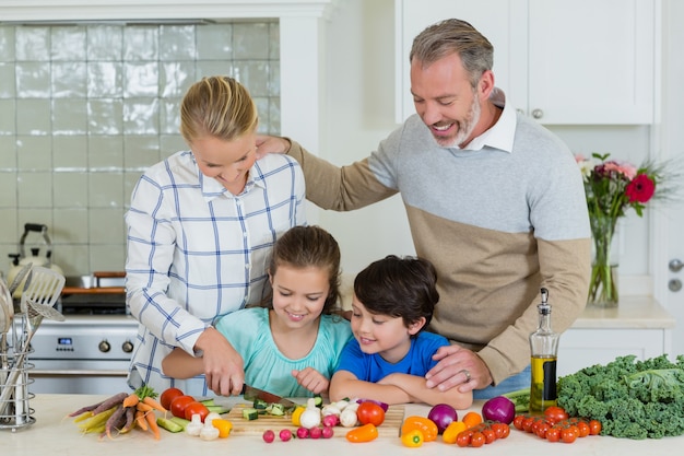 Sorrindo, pais e filhos cortando legumes na cozinha