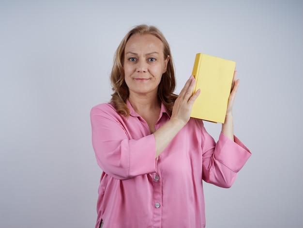 Sorrindo, professora de mulher madura, bibliotecária de camisa rosa, segurando um livro amarelo, olhando. Conceito de educação.