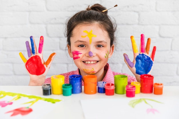 Sorrindo, retrato, de, um, menina, atrás de, a, tabela, com, pintar garrafas, mostrando, dela, mão, e, rosto, pintado, com, cores