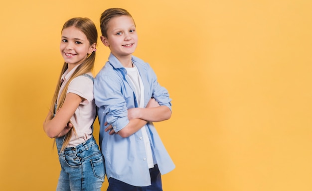 Foto sorrindo, retrato, de, um, menina, e, menino, com, braço cruzou, ficar, costas, contra, fundo amarelo