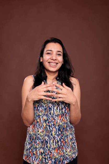 Sorrindo rindo mulher indiana entrelaçando retrato de dedos, olhando para a câmera. Senhora feliz positiva em pé com expressão facial alegre, plano médio de estúdio de vista frontal