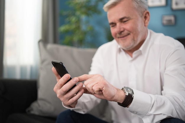 Sorrindo velho sênior falando usando tecnologia moderna de computador de telefone celular em casa