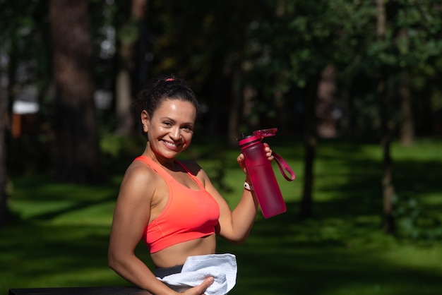 Sorrir fit mulher bebendo água após treino ao ar livre. Manter um bom conceito de hidratação e perda de peso