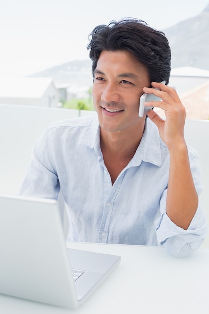 Sorrir homem usando seu laptop e falando no telefone