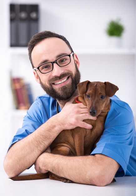 Foto sorrir veterinário masculino está segurando um cachorro.