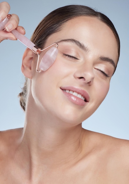 Sorrisão feminina e rolo facial em estúdio para cuidados com a pele beleza e colágeno no rosto em fundo branco Modelo feliz e ferramenta para massagem dermatológica e pele com textura de circulação e bem-estar