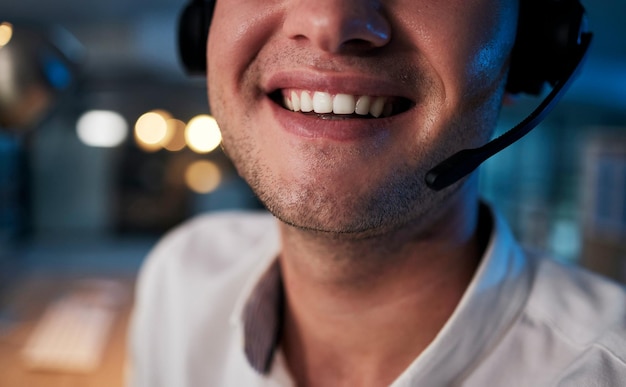 Sorriso de call center e boca de um trabalhador em suporte de telemarketing e negócios de crm em um escritório escuro comércio eletrônico entre em contato conosco e agente de atendimento ao cliente feliz com um fone de ouvido durante o turno da noite