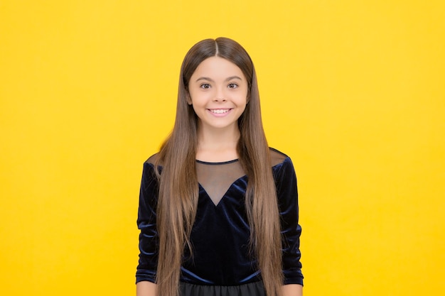 Sorriso de criança feliz com longos cabelos morenos em vestido de moda fundo amarelo infância