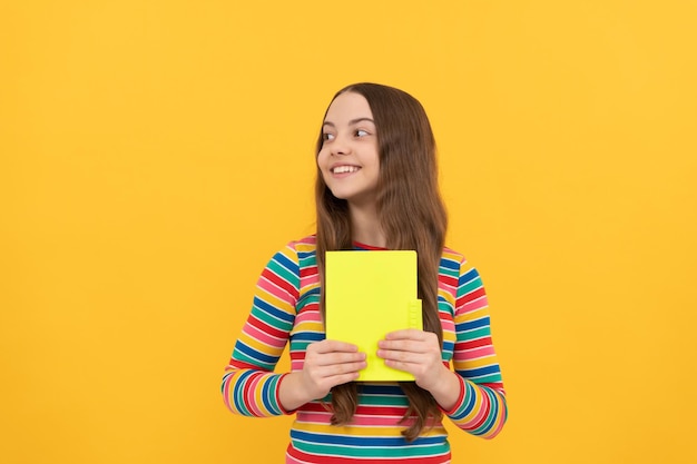 Sorriso de criança menina feliz segurando o livro escola de fundo amarelo