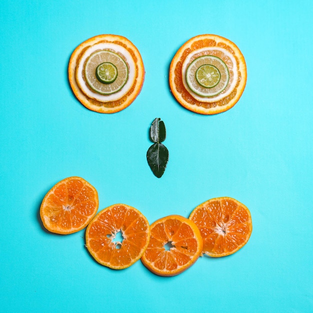 Sorriso de emoticon feito de limões fatiados limas laranja frutas e folhas de limão em fundo azul