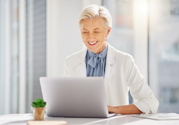 Sorriso de laptop e mulher de negócios sênior no escritório animada para a ideia de pesquisa e plano de missão Projeto on-line e feliz gerente idosa alegre enquanto digita a proposta de navegação e planejamento