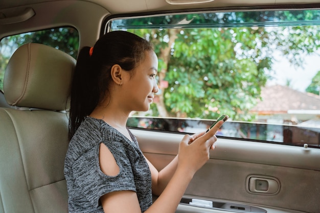 Sorriso de menina segurando um telefone enquanto está sentada no carro com a janela aberta enquanto viaja