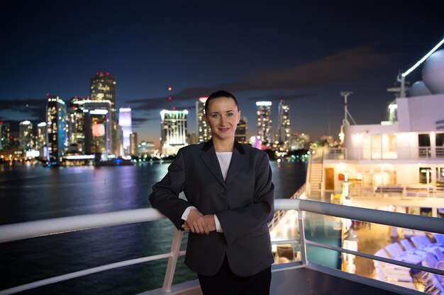 Sorriso de mulher com casaco cinza na varanda na visão noturna do horizonte com iluminação leve em Miami, EUA. Férias de verão, vida noturna, conceito de estilo de vida