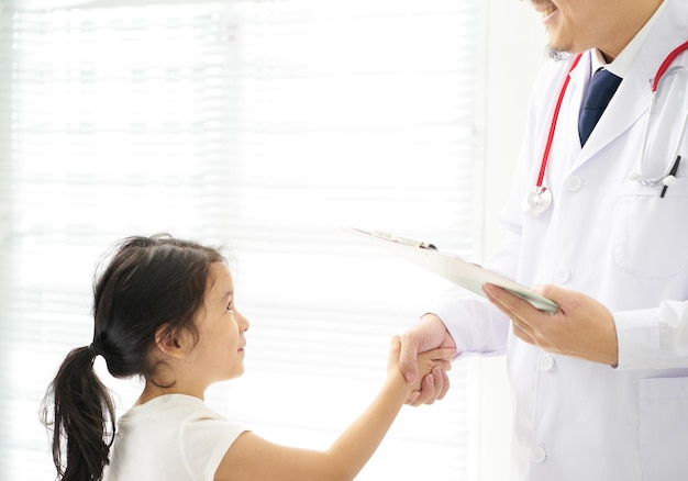 Sorriso desconhecido e médico amigável e garotinha feliz apertando as mãos