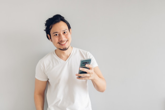 Sorriso e feliz homem de cabelo comprido em camiseta branca casual está usando o smartphone.