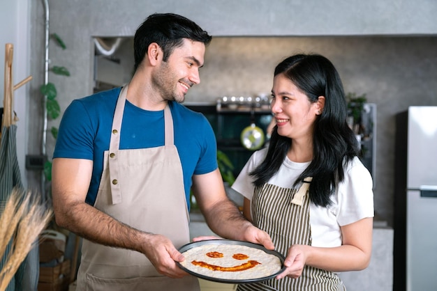 Sorriso feliz, casal apaixonado fez pizza com molho cara divertida na pizza antes de cozinhar fogão ou forno em família relaxa atividade na sala de cozinha com comida e bebida para jantar saudável