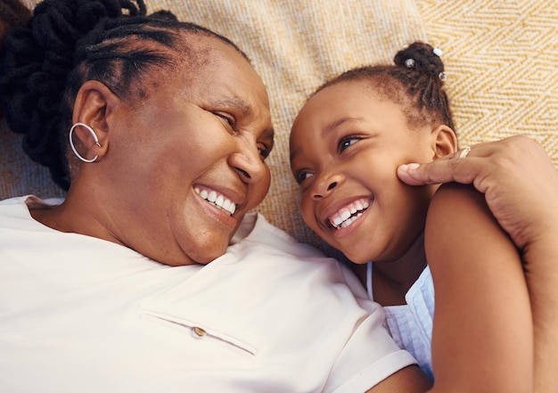 Sorriso feliz e família de uma avó negra e criança em felicidade relaxando e deitada em uma cama em casa Avó africana sênior e garotinha em amor alegre e sorrindo juntos no quarto