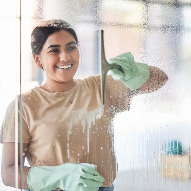 Sorriso feliz e menina limpando janela com frasco de spray e sabão ou detergente empregada doméstica em casa ou hotel Borrão de trabalho doméstico e mulher ou serviço de limpeza profissional lavando vidro no apartamento