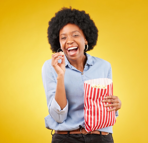 Sorriso feliz e pipoca com mulher negra no estúdio para serviço de streaming de filmes e cinema Comédia e teatro com mulheres e lanches isolados em fundo amarelo para comida, tv e cinema