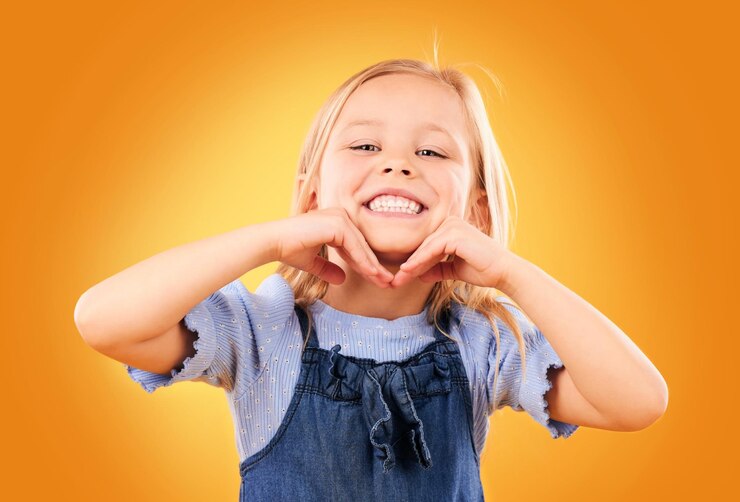 Foto sorriso feliz e retrato de criança em fundo laranja com felicidade alegria e entusiasmo no estúdio infância moda e mãos no rosto de menina em diversão ou roupa da moda estilo jovem e roupas de verão