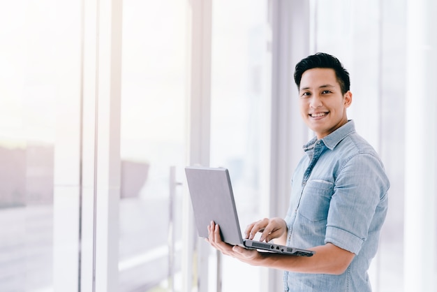 Sorriso feliz homem asiático usando laptop com sentimento positivo no escritório