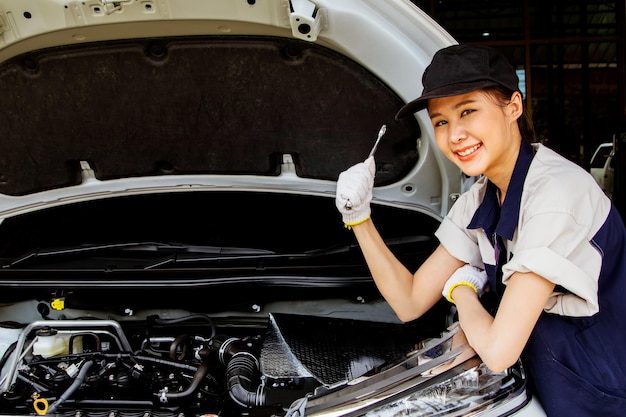 Sorriso feliz linda mulher asiática tailandesa segurando a chave de manutenção inspecionando o carro na garagem.