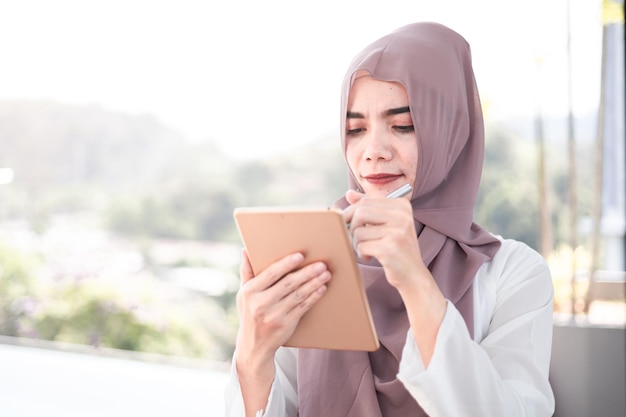 Sorriso feminino muçulmano usando um tablet para o trabalho