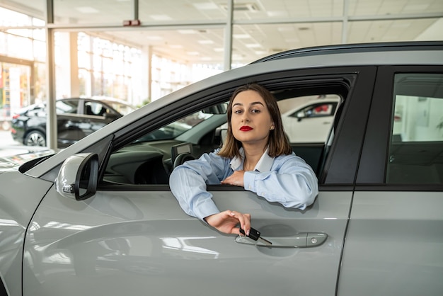 Foto sorriso jovem mulher cliente dentro em novo automóvel moderno e segurando a chave purcase conceito concessionária