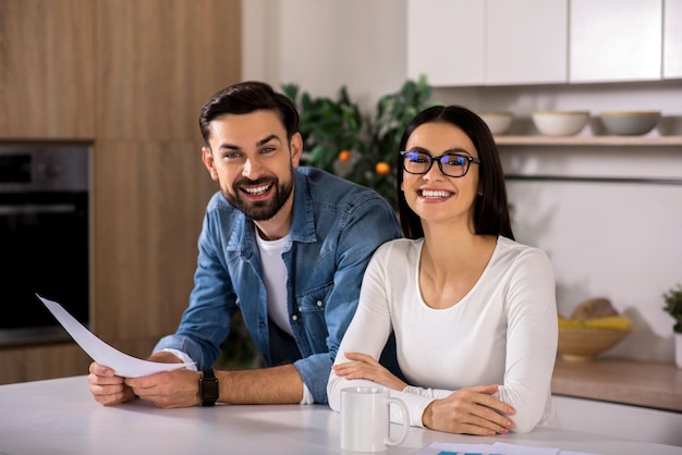 Sorriso largo Casal jovem alegre sentado à mesa e sorrindo na cozinha