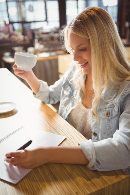 Sorriso loiro bebendo café e escrevendo na folha de papel