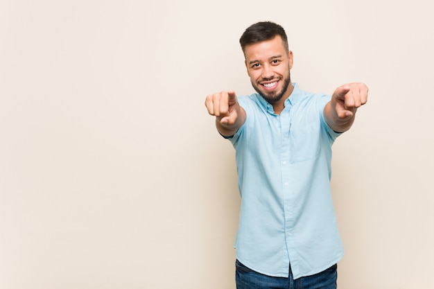 Sorrisos alegres do jovem sul-asiático, apontando para a frente.