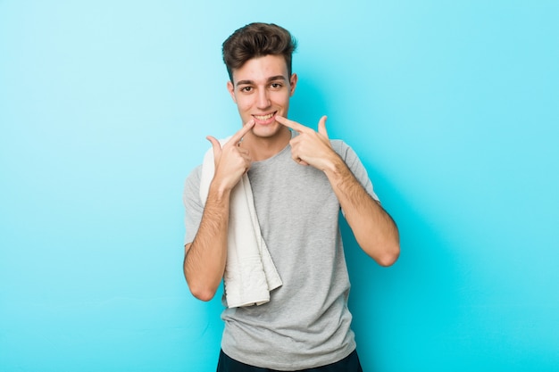 Sorrisos de homem jovem aptidão adolescente, apontando os dedos na boca.