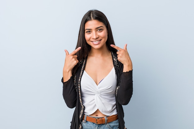 Sorrisos de mulher árabe natural e bonita jovem, apontando os dedos na boca.