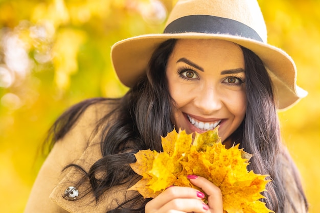Sorrisos muito femininos rodeados pela natureza amarela e segurando as folhas caídas.
