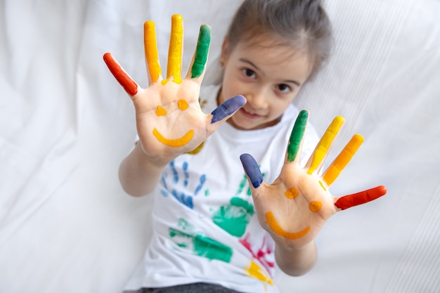 Sorrisos pintados nas mãos de uma menina. Desenhos engraçados brilhantes nas palmas das mãos das crianças.