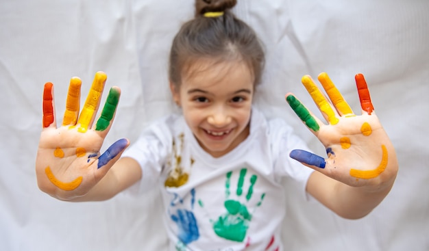 Sorrisos pintados nas mãos de uma menina. Desenhos engraçados brilhantes nas palmas das mãos das crianças.