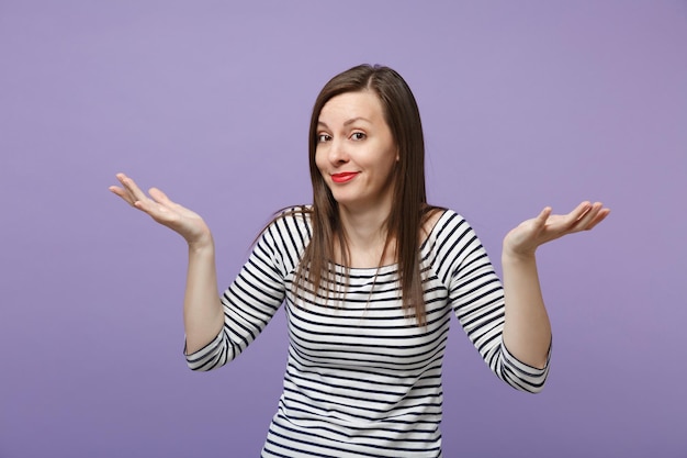 Sorriu zombando menina morena jovem em roupas listradas casuais posando isolado no retrato de estúdio de fundo de parede roxa violeta. Conceito de estilo de vida de pessoas. Mock up espaço de cópia. Espalhando as mãos.