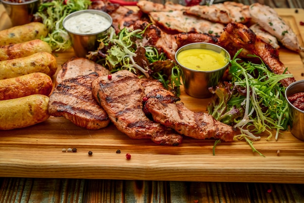 Sortidas deliciosas carnes e legumes grelhados com salada fresca e molho de churrasco na tábua na woode