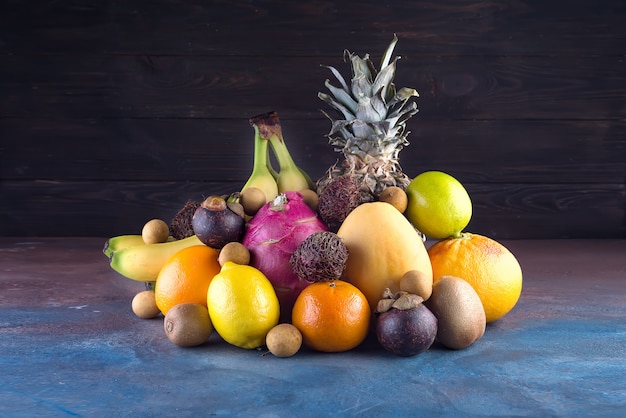 Sortierte tropische Früchte, Orange, Ananas oder Ananas, Kalk, Mango, Drachenfrucht, Orange, Banan, Rambutan und Lichi auf dunklem Hintergrund.