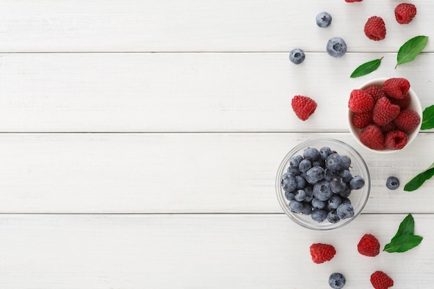 Sortierter Garten und wilder Beerenhintergrund. Mischung aus frischen Bio-Erdbeeren, Himbeeren, Blaubeeren und Brombeeren in Glasschüssel auf weißem Holztisch, Draufsicht, Kopierraum