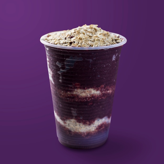 Sorvete brasileiro de açaí e congelado em copo plástico com flocos de aveia. isolado em fundo roxo. Vista frontal do menu de verão.