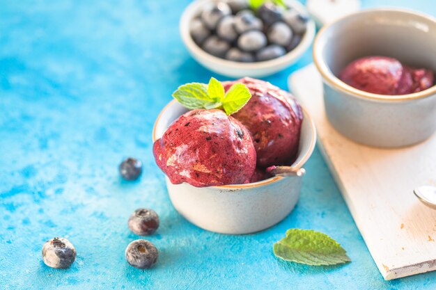 Sorvete caseiro de banana vegan ou gelato com mirtilo em uma tigela sobre fundo azul. Sobremesa saudável.