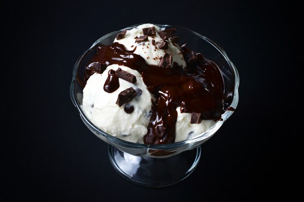 Sorvete de baunilha em uma tigela branca com chocolate em um fundo preto.