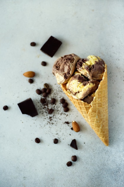 Sorvete de chocolate, baunilha e café em cone de waffle com grãos de café na pedra cinza