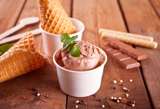 Sorvete de chocolate, cones de waffle, doces na superfície de madeira.